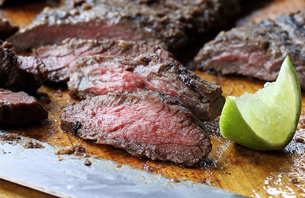 Bistec de falda rebanado sobre una bandeja de metal con gajos de limón agrio.